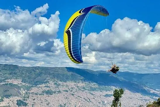 Parapente amarillo y azul volando sobre Medellín